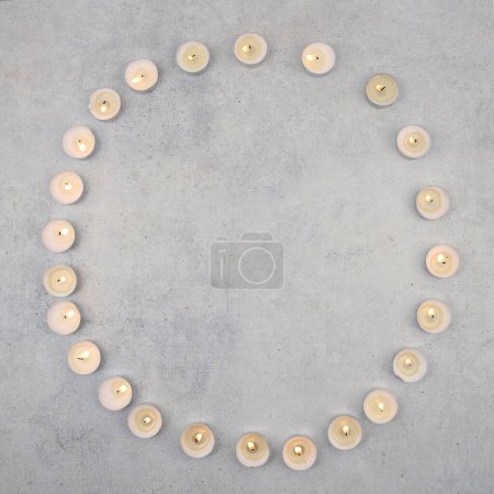 Tea light candles on stone background with copy space. Burning small candles  on cement surface, top view.