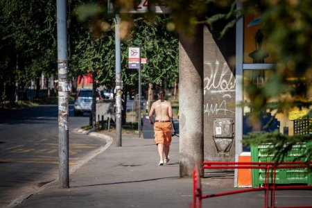 Téléchargez les photos : BELGRADE, SERBIE - 23 JUILLET 2022 : Flou sélectif sur un homme marchant torse nu, torse nu, dans une rue déserte de belgrade lors d'une chaude après-midi d'été lors d'une vague de chaleur en Europe centrale - en image libre de droit