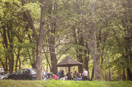 Foto de BELGRADE, SERBIA - 1 DE MAYO DE 2021: Desenfoque selectivo en una familia haciendo un picnic en un parque de Belgrado, comiendo en una mesa de picnic de madera para el Día del Trabajo, una tradición para el 1 de mayo en Serbia - Imagen libre de derechos