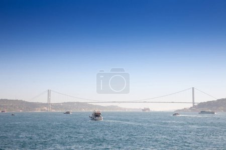 Foto de Puente del Bósforo; también llamado puente de los 15 mártires de julio o de 15 temmuz sehitler koprusu, visto desde lejos con barcos que pasan por el estrecho posporus. es un puente en Estambul que conecta el lado asiático y el europeo. - Imagen libre de derechos