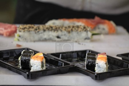 Photo for Selective blur on sushi and sashimi made of salmon and weed in plastic boxes getting prepared to be delivered in a sushi to go takeaway business. - Royalty Free Image