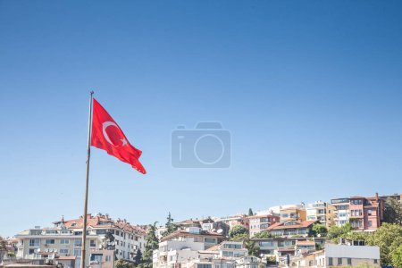 Foto de Bandera turca flotando en el aire frente a un proyecto de desarrollo inmobiliario de casas residenciales en Estambul. También llamada Turk Bayragi, la bandera de pavo, roja con una media luna blanca, es el símbolo nacional de la república de pavo. - Imagen libre de derechos