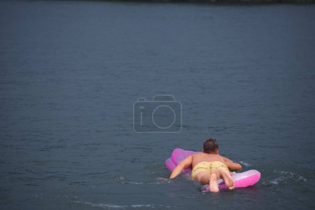 Foto de BELGRADA, SERBIA - 31 DE JULIO DE 2021: Desenfoque selectivo en un hombre joven, caucásicos blancos, nadando y flotando en un colchón de aire en el río Reka Sava en Obrenovac, Belgrado. - Imagen libre de derechos