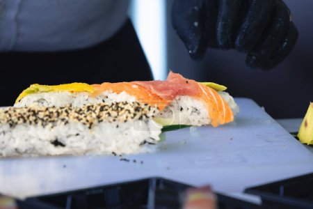 Foto de Desenfoque selectivo en las manos de un chef que prepara sushi y sashimi hecho de salmón, preparándose para ser entregado en un sushi para llevar. - Imagen libre de derechos