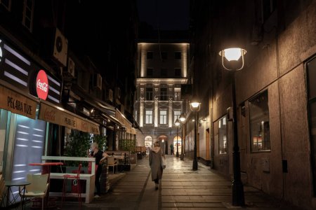 Foto de BELGRADE, SERBIA - 21 de enero de 2023: Desenfoque selectivo en la calle Marka Leka con una mujer caminando sola por la noche en una calle vacía. Es una calle peatonal y atracción turística de la ciudad, en el distrito de Stari Grad. - Imagen libre de derechos