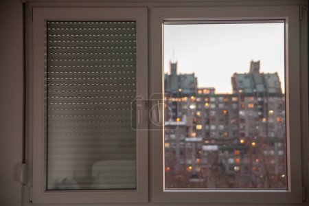Téléchargez les photos : Flou sélectif sur les fenêtres en PVC, en plastique, l'un recouvert de volets roulants, dans un environnement urbain de Serbie avec des bâtiments résidentiels de grande hauteur en arrière-plan. - en image libre de droit