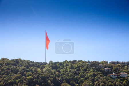 Foto de Panorama de una colina con madera, naturaleza y bosque con bandera turca flotando en el aire frente a un cielo azul en Estambul. También llamada Turk Bayragi, la bandera de pavo, roja con una media luna blanca, es el símbolo nacional de la república de pavo.. - Imagen libre de derechos
