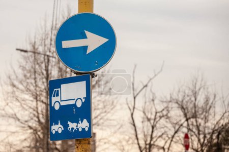 Téléchargez les photos : Flou sélectif sur un panneau routier, cercle bleu avec flèche blanche pointant à droite, indiquant que la route est obligatoire pour les camions, les tracteurs et les chariots à chevaux. - en image libre de droit