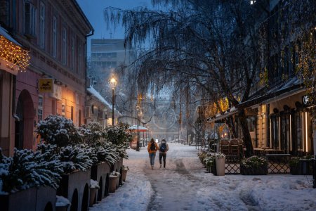 Téléchargez les photos : PANCEVO, SERBIE - 12 DÉCEMBRE 2021 : Flou sélectif sur deux personnes, marchant dans la neige sur la rue principale de Pancevo, lors d'une nuit neigeuse hivernale dans la région de Banat. - en image libre de droit