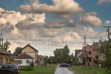 Téléchargez les photos : ALIBUNAR, SERBIE - 8 AOÛT 2019 : Panorama d'une rue rurale typique d'un village rural, Alibunar, en Serbie, Voïvodine, avec une voiture passant par là, en été. Alibunar est un village de Banat. - en image libre de droit