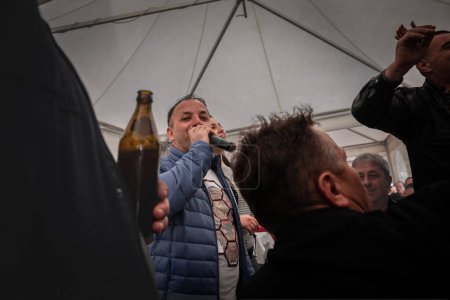 Photo for KACAREVO, SERBIA - FEBRUARY 18, 2023: Selective blur on man, a serbian singer, performing in a kafana, a traditional serbian restaurant and bar, with people drinking beer around while celebrating. - Royalty Free Image