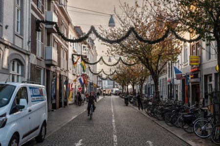 Photo for MAASTRICHT, NETHERLANDS - NOVEMBER 10, 2022: People biking on Hoenderstraat street, Maastricht city center, a pedestrian street surrounded by shops and stores with recently added christmas decorations. - Royalty Free Image
