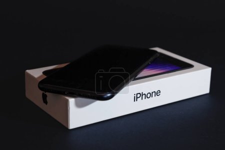 Foto de BELGRADE, SERBIA - 28 DE MARZO DE 2023: Captura de estudio de un Iphone SE3 negro, completamente nuevo, con su caja aislada sobre fondo negro. Lanzado en 2022, IPhone SE 3 es la tercera generación de Apple. - Imagen libre de derechos