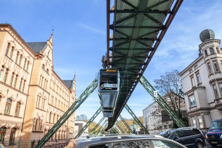 Foto de WUPPERTAL, ALEMANIA - 11 DE NOVIEMBRE DE 2022: Desenfoque selectivo en el tren que pasa por el Wuppertal schwebebahn, el icónico ferrocarril de suspensión de la ciudad con un atasco de tráfico de coches por debajo. - Imagen libre de derechos