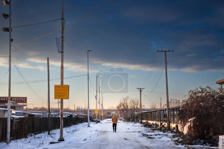 Téléchargez les photos : PANCEVO, SERBIE - JANVIER 23, 2023 : Panorama d'une rue gelée avec de la neige avec un homme marchant seul dans une rue recouverte de glace à Pancevo au crépuscule. L'hiver en Serbie peut être froid. - en image libre de droit