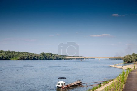 Téléchargez les photos : Focus sélectif sur un petit bateau sur le Danube sur le fleuve Serbia Croatia avec le pont ilok backa palanka en arrière-plan, un important passage frontalier entre l'Union européenne et la Serbie. - en image libre de droit