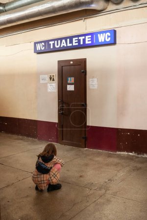 Téléchargez les photos : RIGA, LETTONIE - 23 AOÛT 2022 : Flou sélectif sur une jeune fille, accroupie, attendant des toilettes devant les toilettes publiques du marché central de Riga, Centraltirgus. - en image libre de droit