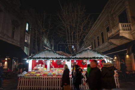Téléchargez les photos : BELGARDE, SERBIE - 2 JANVIER 2023 : Flou sélectif Boutiques du marché de Noël de Belgrade avec des gens qui passent dans le flou de la vitesse sous la neige la nuit, sur la rue Kneza Mihailova, en Serbie. - en image libre de droit