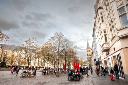 Foto de BONN, ALEMANIA - 7 DE NOVIEMBRE DE 2022: Multitud de personas caminando por tiendas y tiendas en la plaza Munsterplatz, a la plaza principal y calle del centro de la ciudad de Bonn, en el oeste de Alemania. - Imagen libre de derechos