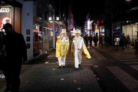 Photo for COLOGNE, GERMANY - NOVEMBER 11, 2022: Selective blur on a group of two men, friends, german men dressed with white costumes for Cologne Carnival walking at night in Cologne center. - Royalty Free Image