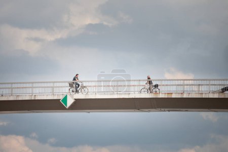 Photo for SREMSKA MITROVICA, SERBIA - JUNE 10, 2023: Men riding bicycles in the city center of Sremska Mitrovica, on the Most svetog irineja bridge, during a cloudy afternoon, over sava river. - Royalty Free Image