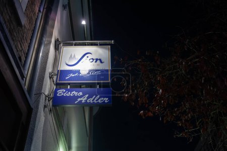Foto de AACHEN, ALEMANIA - 8 DE NOVIEMBRE DE 2022: Desenfoque selectivo en un logotipo de Sion Beer en un minorista local de Aquisgrán por la noche. Sion es una cerveza Kolsch, una cerveza tradicional de la región de Colonia. - Imagen libre de derechos