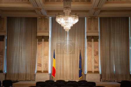 Foto de BUCHAREST, RUMANIA - 13 DE MARZO DE 2023: Desenfoque selectivo de la bandera rumana y la bandera de la unión europea en una sala de conferencias vacía en el palacio del parlamento rumano, símbolo de Bucarest del comunismo rumano. - Imagen libre de derechos