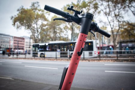 Téléchargez les photos : Flou sélectif sur un scooter électrique rose à louer, disponible dans les rues de Cologne, en Allemagne, devant un bus de transports publics, appartenant à une société de technologie spécialisée dans le partage de véhicules. - en image libre de droit
