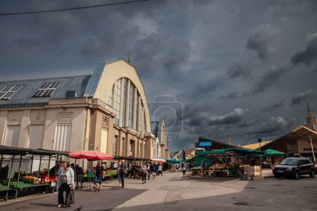 Foto de RIGA, Letonia - 23 de agosto de 2023: Panorama del mercado verde frente a los edificios de Centraltirgus, mercado central de Riga, un hito y un símbolo de la economía letona, durante una tarde nublada y lluviosa. - Imagen libre de derechos
