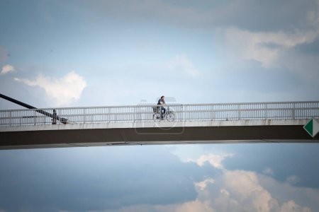 Photo for SREMSKA MITROVICA, SERBIA - JUNE 10, 2023: man riding a bicycle in the city center of Sremska Mitrovica, on the Most svetog irineja bridge, during a cloudy afternoon, over sava river. - Royalty Free Image