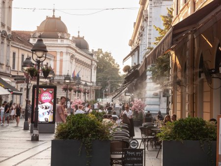Photo for BELGRADE, SERBIA - AUGUST 14, 2023: Crowd of people sitting at the terrace of a Belgrade Bar Cafe, being cooled with a cooling mist terrace cooler for summer using droplets on Knez Mihailova street. - Royalty Free Image