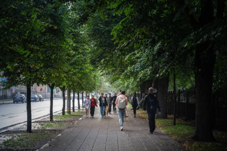 Téléchargez les photos : RIGA, LETTONIE - 23 AOÛT 2023 : Une foule sélective brouille les pistes dans une rue verdoyante de Riga par un après-midi pluvieux. Riga est la capitale de la Lettonie et le principal centre des États baltes. - en image libre de droit