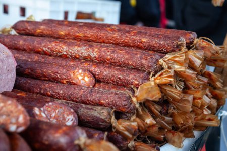 Photo for Selective blur on cajna kobasica sausages spiked for sale on a stand of a serbian market. Cajna kobasica, or tea sausage, is a traditional serbian sausage made of smoked cured pork. - Royalty Free Image