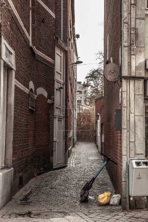 Téléchargez les photos : LIEGE, BELGIQUE - 9 NOVEMBRE 2022 : Flou sélectif sur un scooter électrique dans une rue étroite et sale de Liège, en Belgique, piétonne, avec des sacs poubelles autour. - en image libre de droit