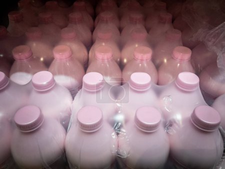 Selective blur on Plastic bottles of yogurt in warehouse packaging, ready for distribution and shipment, pink color, wrapped in plastic. Dairy logistics and bulk storage concept.