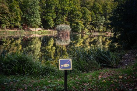 No fishing sign in front of a Panorama of the pond Jankovac, a small water lake surrounded by trees and forest in the Papuk mountain, a major national park of Croatia, in the Slavonia region.