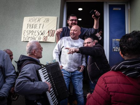 Foto de BELO BLATO, SERBIA - 3 DE FEBRERO DE 2024: Músicos serbios, una banda hecha de acordeonista y otros instrumentos tocando frente a la gente animando, felices en un día de mercado en kobasicijada belo blato. - Imagen libre de derechos