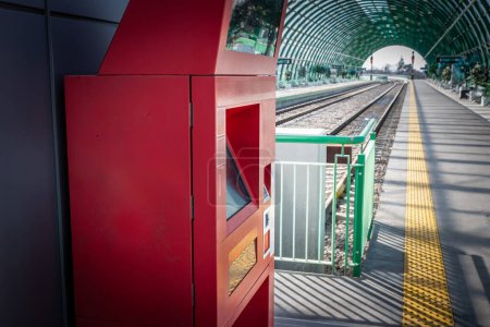 Foto de Desenfoque selectivo en una máquina expendedora de billetes de tren rojo, listo para vender billetes de tren en una estación de tren, junto a las plataformas y la vía, al estilo europeo. - Imagen libre de derechos