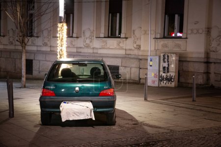 Photo for BELGRADE, SERBIA - DECEMBER 1, 2023: car parked on a side walk, not abiding by regulations, with a licence plate covered to try avoiding fines, breaking the rules, at night, in belgrade. - Royalty Free Image