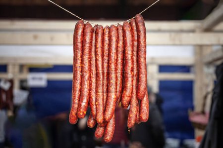 Photo for Selective blur on cajna kobasica sausages spiked for sale hanging on a stand of a serbian market. Cajna kobasica, or tea sausage, is a traditional serbian sausage made of smoked cured pork. - Royalty Free Image