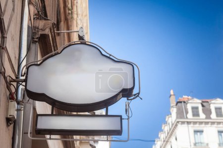 Selektive Unschärfe auf einem leeren weißen Ladenschild, das an einer Hausfassade hängt, sichtbar vor klarem Himmel in einer französischen Stadtstraße, ideal für Einzelhandelswerbung & städtische Gewerbeschau.