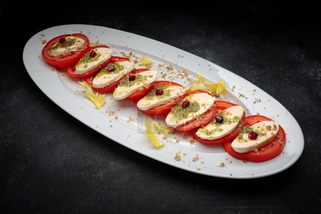 Photo for Sliced tomatoes with cheese and garlic sauce on a plate, on dark concrete - Royalty Free Image