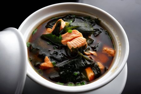 Sopa de miso con salmón, algas y cebollas, sobre fondo negro