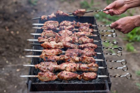 Téléchargez les photos : He flips the fried shish kebab on the grill with his hands on the skewers. low depth of field - en image libre de droit