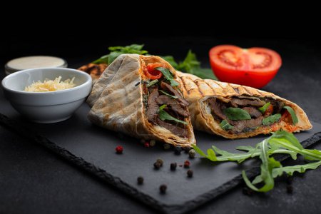 Shawarma with meat, cheese, tomatoes and sauce, on a black background with entourage