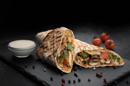 Téléchargez les photos : Viande juteuse et légumes frais enveloppés dans un shawarma classique, servi avec une sauce savoureuse - en image libre de droit