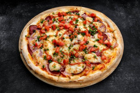Foto de Pizza deliciosamente cursi con carnes ahumadas, tomates, salchichas y ketchup. Sobre un fondo oscuro - Imagen libre de derechos