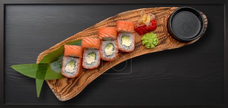 Téléchargez les photos : Rouleau de sushi avec saumon, fromage crémeux et avocat sur fond de bois foncé - en image libre de droit