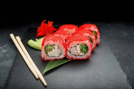 Foto de Rollo de sushi con palitos de cangrejo, queso crema, aguacate y caviar sobre un fondo negro con jengibre y wasabi - Imagen libre de derechos