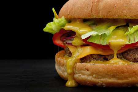 Hamburger close-up with beef, tomato, lettuce, cheese on a black background. Fastfood on dark background with place for your text